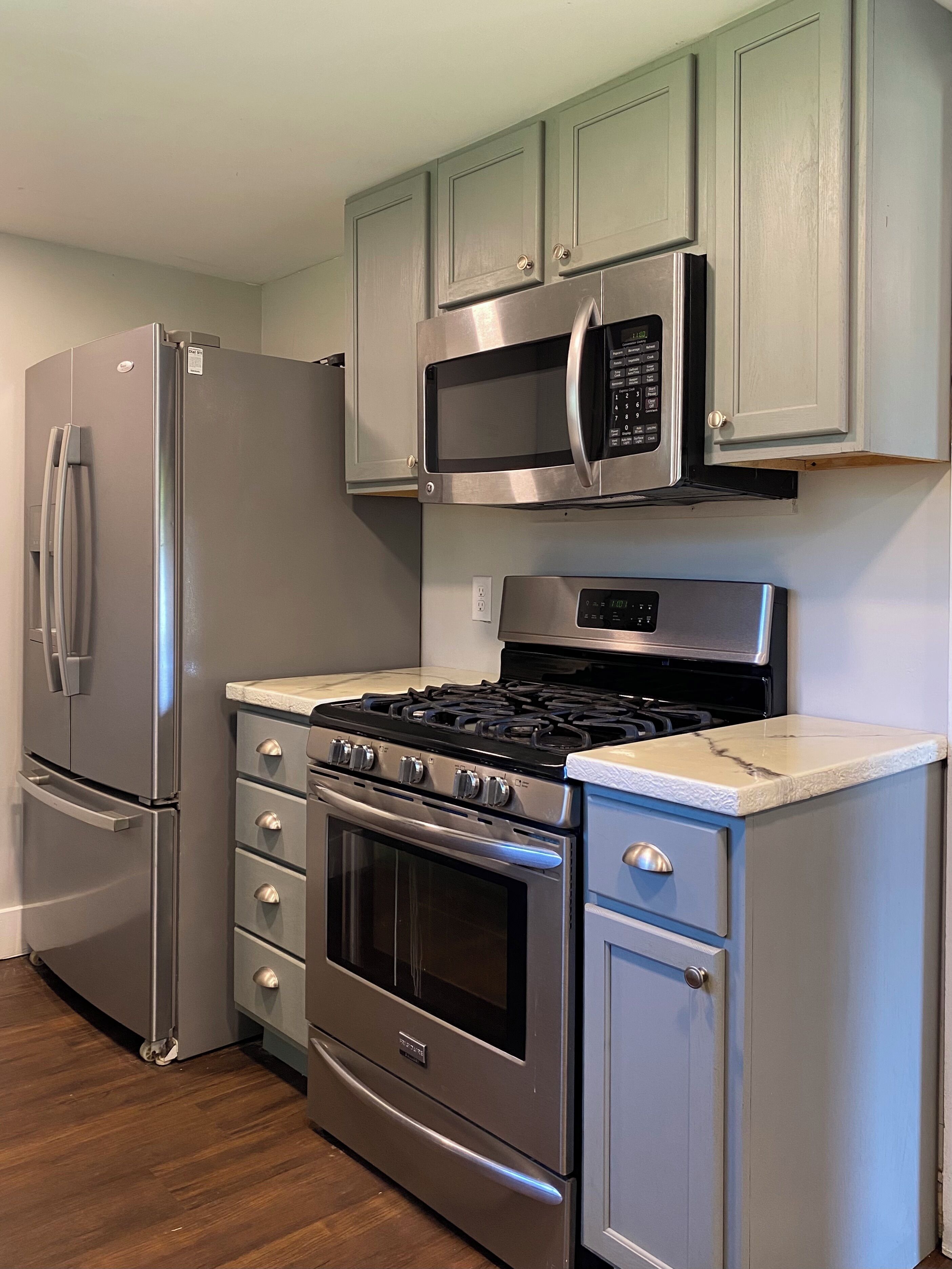 A kitchen with a stainless steel refrigerator, microwave, stove, oven, and a set of drawers.