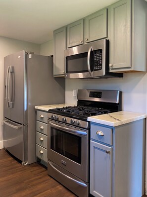 A kitchen with a stainless steel refrigerator, microwave, stove, oven, and a set of drawers.