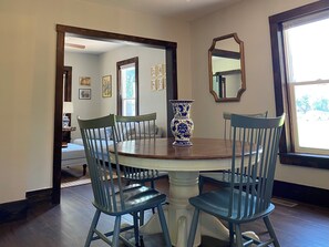 A dining area with a round table, four chairs, a vase, and framed pictures on the walls.