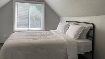 A single bed with a metal frame in a room with a sloped ceiling and a window with blinds.