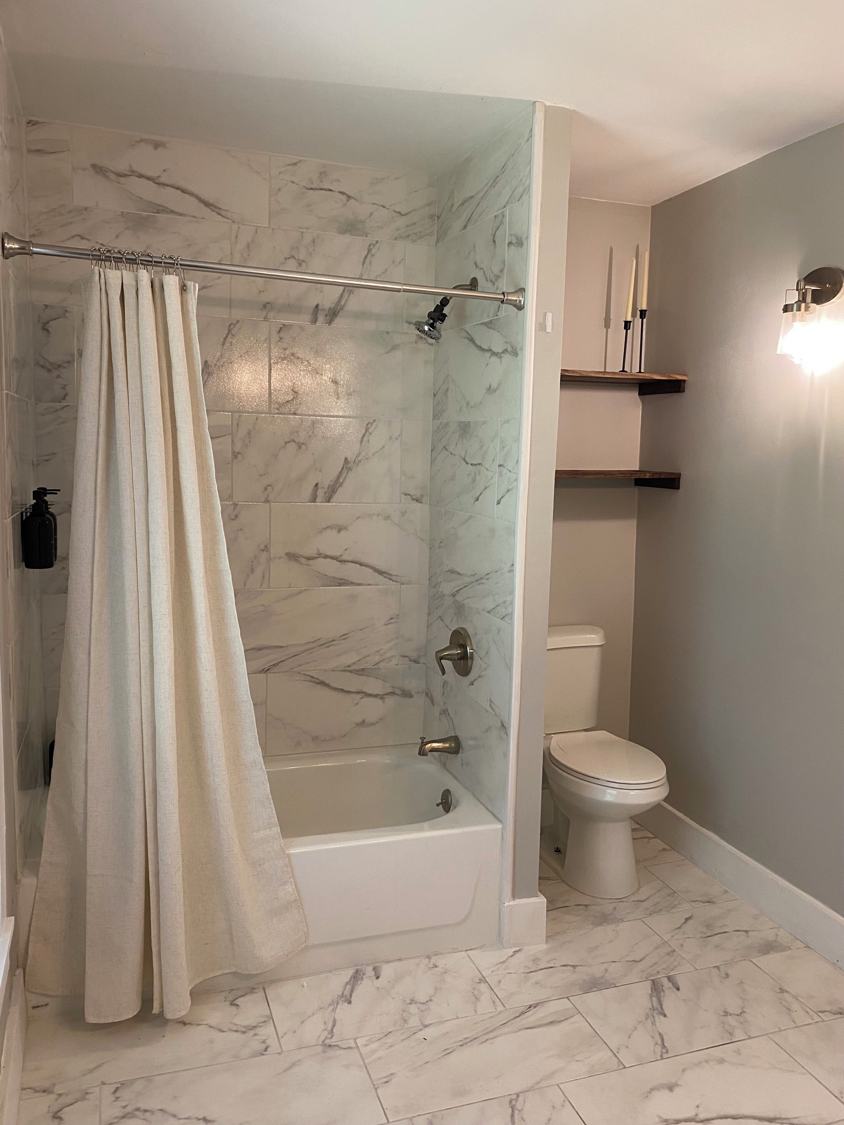 A bathroom with a shower, toilet, and bathtub, all with marble tiles.