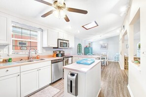 Une cuisine moderne avec des meubles blancs, un four à micro-ondes encastré et un ventilateur de plafond.