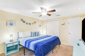 A bedroom with a bed, nightstand, ceiling fan, and a door. - Pleasant beach home with central AC, deck & work space - walk to beach & dining (Tybee Island)