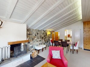 Een ruime woonkamer met een stenen muur, een open haard en een eethoek met stoelen en tafels.