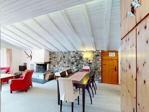 Een gezellige woonkamer met een open haard, stenen muur en een eethoek met een houten tafel en stoelen.