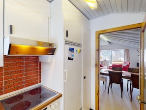 Een kleine keuken met een kookplaat, een koelkast en een eethoek met een tafel en stoelen.