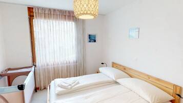A hotel room with a bed, a desk, a chair, a hanging light fixture, and a window with curtains.