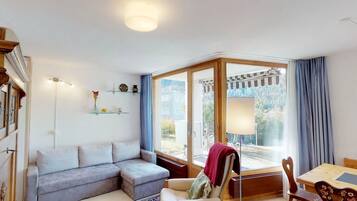 A modern living room with a sectional sofa, a dining table with chairs, and a large sliding glass door leading to an outdoor area.