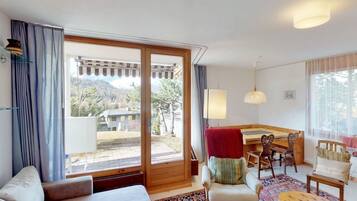 A room with a sofa, a dining table with chairs, a patterned rug, and a view of a mountainous landscape through a large sliding glass door.
