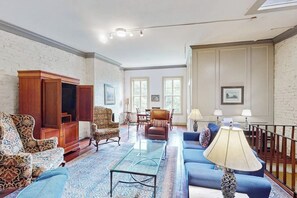 A spacious living room with a large wooden cabinet, a patterned sofa, a blue sofa, and a glass coffee table. - Historic downtown gem - walk to SCAD/City Market/Forsyth Park (Savannah)