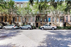 Une rangée de maisons de ville en briques, avec une allée pavée, des arbres et des voitures garées.
