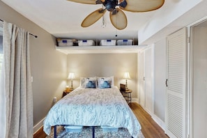 Une chambre à coucher avec un lit, deux lampes de chevet, un ventilateur de plafond et une fenêtre avec des rideaux.