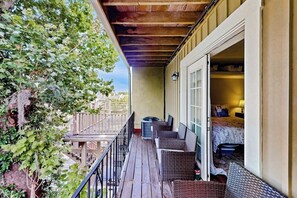Ein Balkon mit Korbmöbeln, ein Bett mit gemustertem Überwurf und Blick auf einen Baum.