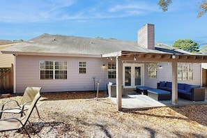 Une maison de plain-pied dotée d’un patio couvert, d’une cheminée et d’une petite terrasse aménagée avec du mobilier d’extérieur.