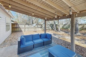 A covered outdoor seating area with a wicker sofa and ottoman, a patterned rug, and a wooden ceiling with hanging lights. - Well-appointed home with spacious backyard, firepit, streaming, & central AC (Savannah)