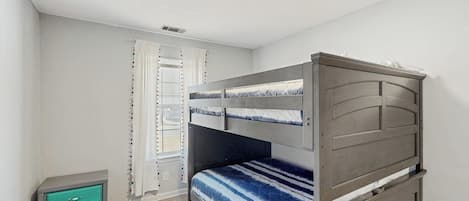 Una habitación con literas, un pequeño archivador verde y una ventana con cortinas.