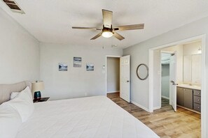 A bedroom with a bed, a ceiling fan, a nightstand, a lamp, and a door leading to a bathroom. - Well-appointed home with spacious backyard, firepit, streaming, & central AC (Savannah)