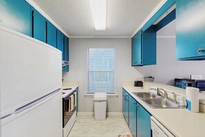 Eine kleine Küche mit Kühlschrank, Backofen, Spüle und Fenster.