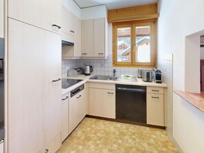 Eine kleine Küche mit Geschirrspüler, Herd und einem Fenster mit Blick auf ein Haus.