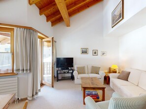 Ein Wohnzimmer mit Fernseher, weißen Sofas, einem Couchtisch und einer Holzbalkendecke.