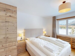 Ein Hotelzimmer mit einem Bett, zwei Nachttischlampen, einem Holzschrank und einem Fenster mit Blick auf eine verschneite Landschaft.