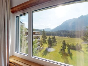 Ein Zimmer mit großem Fenster mit Blick auf eine Wiese und Berge.