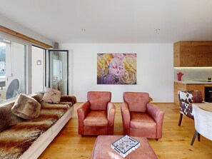 Ein modernes Wohnzimmer mit einer Couch, zwei Sesseln, einem Couchtisch und einem Gemälde an der Wand.