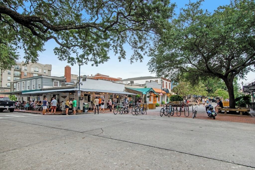 A street scene with outdoor seating at cafes, bicycles parked along the sidewalk, and a tree providing shade.