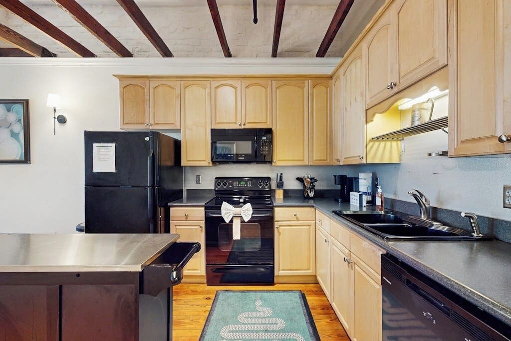 A kitchen with wooden cabinets, a black refrigerator, a microwave, a stove with a bow, and a dishwasher.