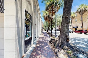A sidewalk with a brick pattern, trees, and a building with large windows. - Charming loft near City Market with washer/dryer, AC - walk to river (Savannah)