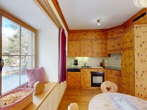 A kitchen with wooden cabinets, a dishwasher, and a window overlooking a snowy landscape. - Apartment Domiziana by Interhome (Samedan)