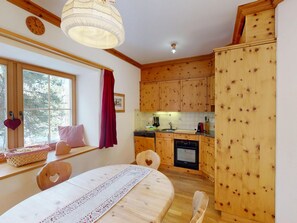 Eine gemütliche Küche mit Holzausstattung, einem Esstisch mit Spitze und einem Fenster mit Blick auf Bäume.