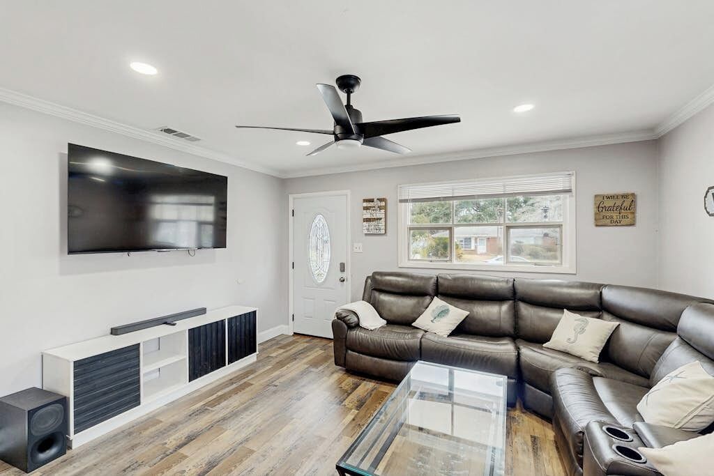 A modern living room with a leather sofa, a glass coffee table, a mounted TV, and a ceiling fan.