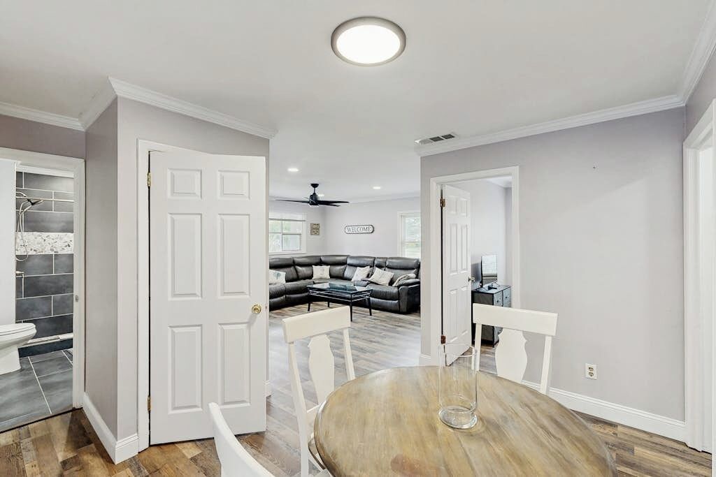 Uma sala de estar moderna com um sofá seccional, uma mesa de jantar com cadeiras e uma cozinha visível através de uma porta aberta.