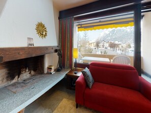 Ein Wohnzimmer mit einem roten Sofa, einem Kamin, einem Fenster mit Blick auf eine Bergstadt und einer Wanddekoration in Sonnenform.