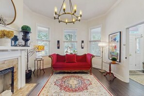 A spacious living room with a red sofa, a large ornate rug, and a fireplace. - Charming Victorian home with modern comforts & steps from parks (Savannah)
