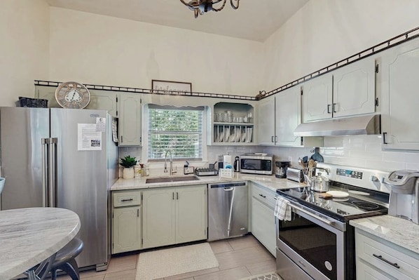 A modern kitchen with stainless steel appliances, a dining area with a round table, and a window with blinds. - Charming Victorian home with modern comforts & steps from parks (Savannah)