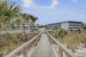 A wooden boardwalk leading to a beachfront hotel with multiple balconies. - Waterfront island getaway with balcony, pool, tennis, & easy beach access (Tybee Island)