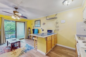 A compact kitchen with a central island, a dining area with a table and chairs, and a large sliding glass door leading to an outdoor space. - Waterfront island getaway with balcony, pool, tennis, & easy beach access (Tybee Island)