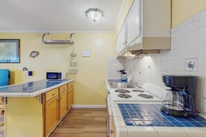 A kitchen with a microwave, stove, and coffee maker. There is a sink and cabinets. - Waterfront island getaway with balcony, pool, tennis, & easy beach access (Tybee Island)