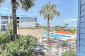 A pool area with lounge chairs and umbrellas, surrounded by palm trees and a building with balconies. - Waterfront island getaway with balcony, pool, tennis, & easy beach access (Tybee Island)