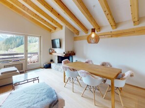 Ein modernes Interieur mit einem Holzesstisch, weißen Stühlen, einem Kamin und einem an der Wand befestigten Fernseher.