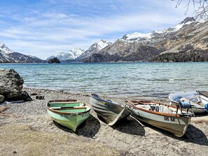 Tre imbarcazioni su una riva rocciosa affacciata su un lago, con montagne sullo sfondo.