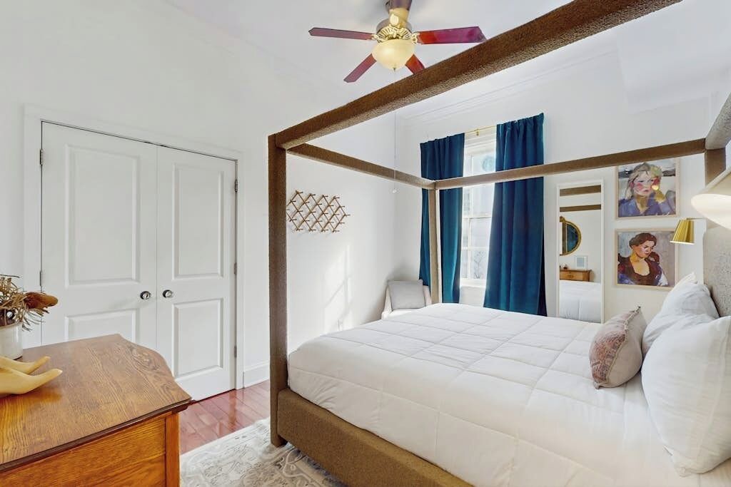 Un lit à baldaquin avec un cadre en bois, un ventilateur de plafond et une porte blanche.