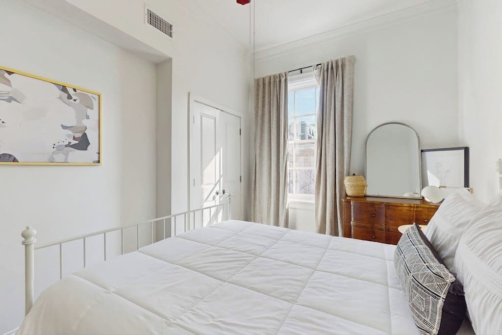 Un dormitorio con cama, cómoda, espejo y ventana con cortinas.