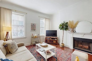 A living room with a sofa, coffee table, television, fireplace, and decorative plants. - Charming, historic condo w/ a full kitchen, free WiFi, & central A/C (Savannah)