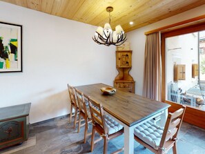 Una zona de menjador amb taula de fusta, cadire cuscidors, un penjallum i un armari amb un rellotge.