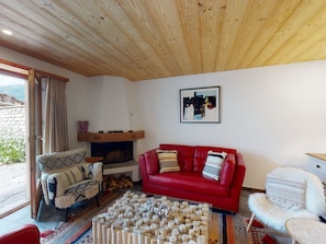 Ein gemütliches Wohnzimmer mit einem roten Sofa, einem gemusterten Sessel, einem Glastisch und einem Kamin.