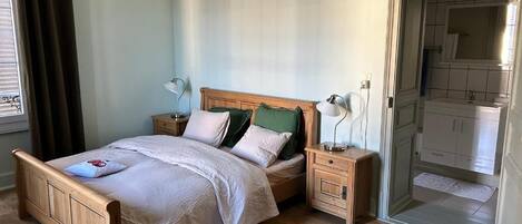 A bedroom with a wooden bed, bedside tables, a nightstand, and a view of the bathroom.