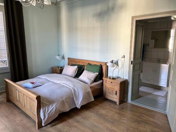A bedroom with a wooden bed, bedside tables, a nightstand, and a view of the bathroom.